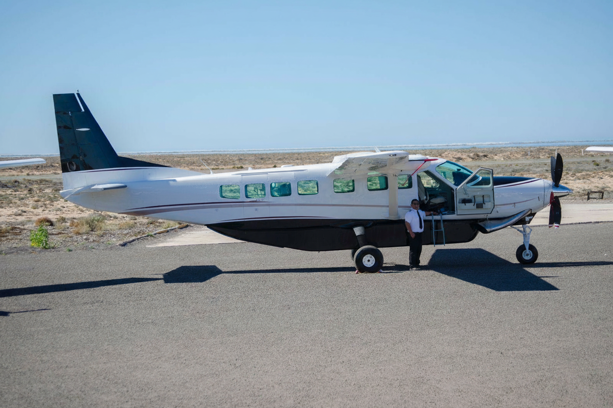 Pilot stands by a white twin-engine turboprop airplane on a tarmac.