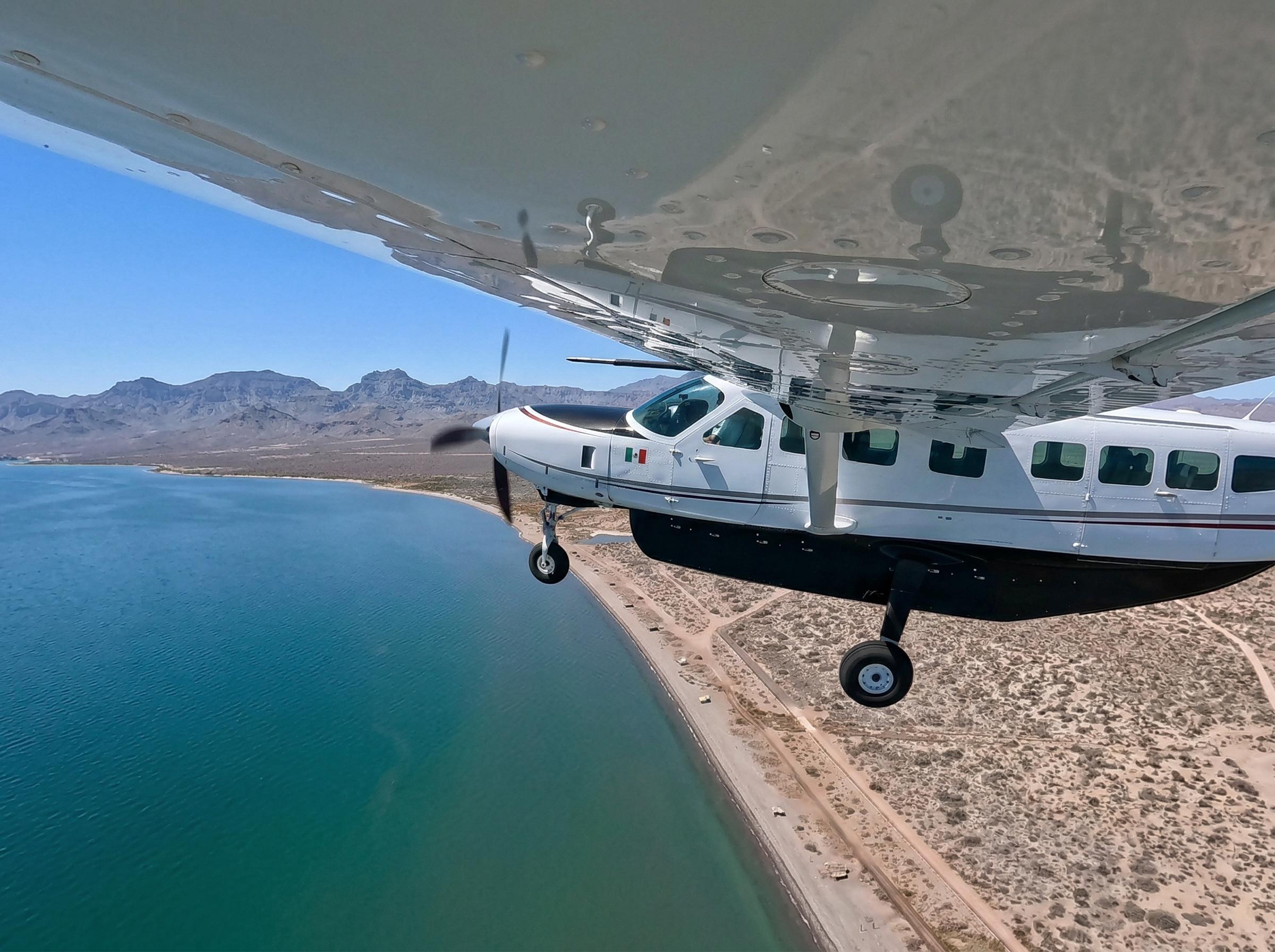 Private charter flight over the Baja California coastline — Cessna Grand Caravan flying above turquoise Sea of Cortez waters