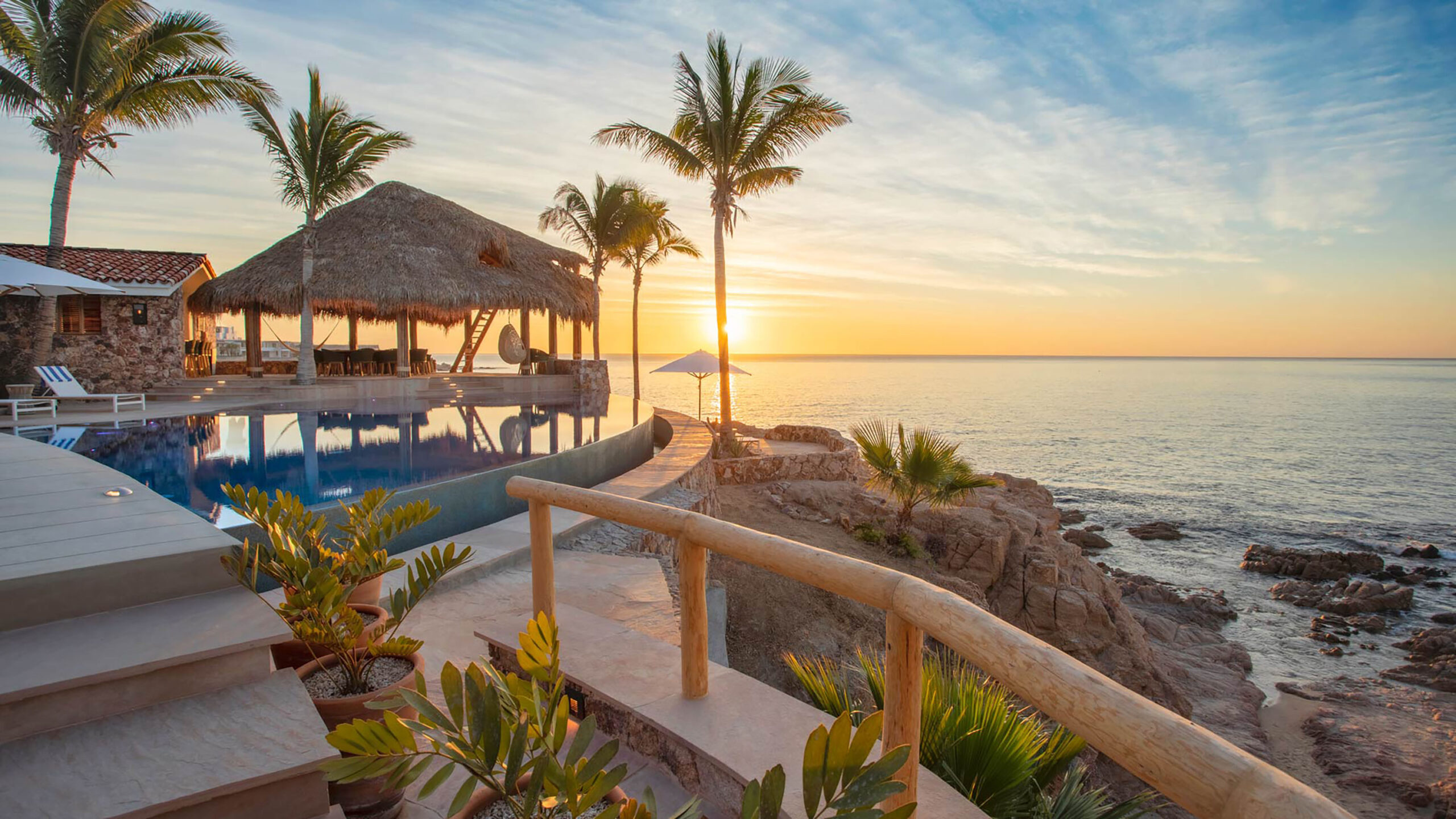 Casa Cielito del Mar beachfront property with infinity pool, thatched palapa, and palm trees overlooking the ocean at sunset, offering direct waterfront ac