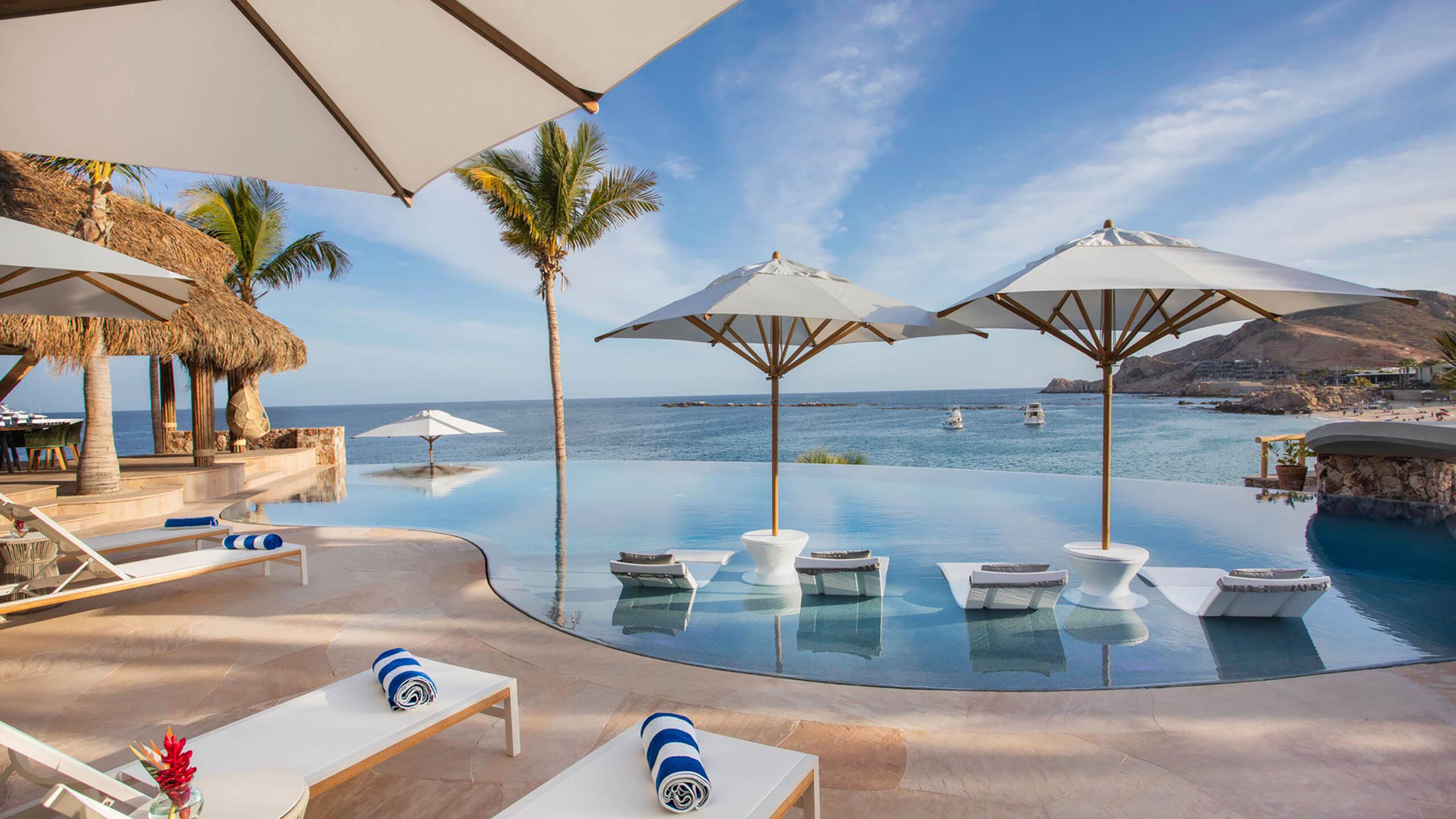 Casa Cielito del Mar an infinity pool overlooking the ocean, featuring in-water lounge chairs under white umbrellas. Relax poolside with tropical palms swa