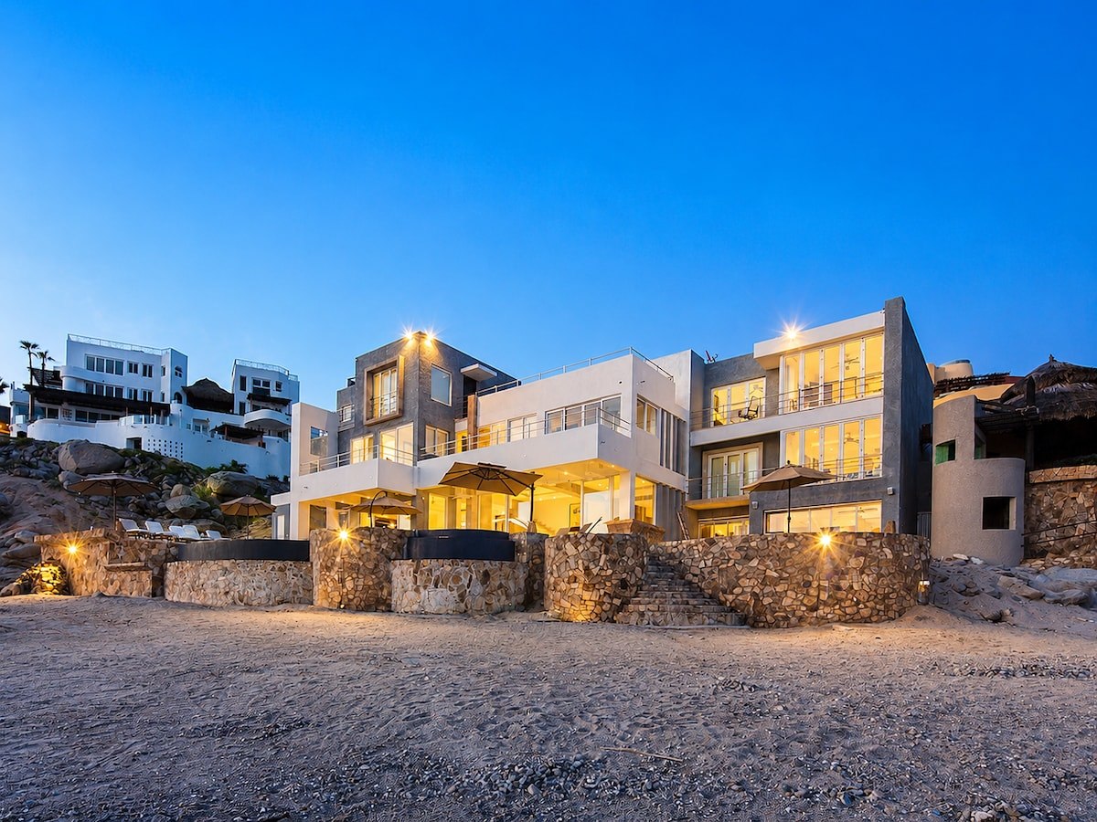 Modern oceanfront exterior of Casa Luna illuminated at dusk beside the rocky Cabo shoreline